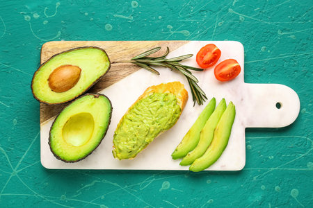 Board with delicious avocado toast, rosemary and tomatoes on green background