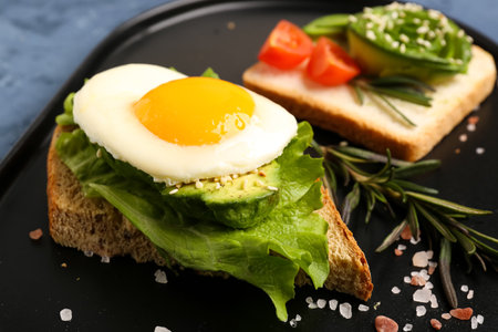 Delicious avocado toast with fried egg on black plate, closeup