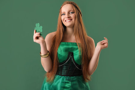 Beautiful redhead woman with paper clover on green background. St. Patrick's Day celebrationの写真素材