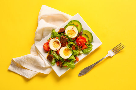 Plate of delicious salad with boiled eggs and salmon on yellow background