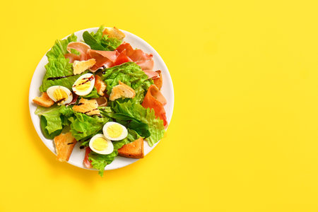 Plate of delicious salad with boiled eggs and jamon on yellow backgroundの写真素材