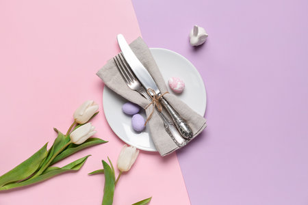 Table setting with Easter eggs and tulips on color background