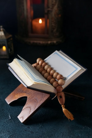 Rehal with Koran and prayer beads for Ramadan on dark table, closeup
