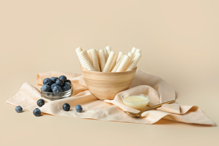 Bowl delicious wafer rolls, condensed milk and blueberries on beige backgroundの写真素材