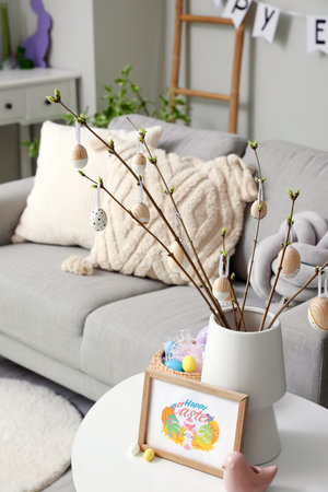 Vase with tree branches, Easter eggs and greeting card on table in living room