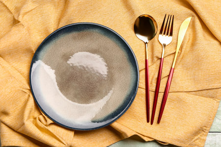 Yellow tablecloth with plate and set of cutlery on green wooden backgroundの写真素材