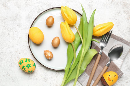 Table setting with Easter eggs, cutlery and tulip flowers on white grunge background