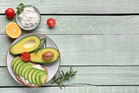 Plate with delicious avocado toast, tomatoes, orange and cream cheese on green wooden backgroundの写真素材