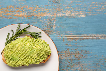 Plate with delicious avocado toast and rosemary on blue wooden background