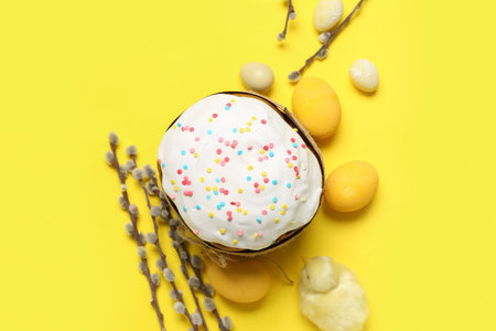 Composition with tasty Easter cake, painted eggs, willow branches and toy chick on yellow backgroundの写真素材