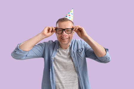 Mature man in funny disguise on lilac background. April Fools' Day celebrationの写真素材