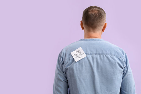 Sticky paper with text HAPPY FOOL'S DAY on back of mature man against lilac background