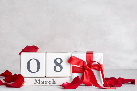 Cube calendar with date MARCH 8, gift box and rose petals on table near gray wall. Women's Day celebrationの写真素材