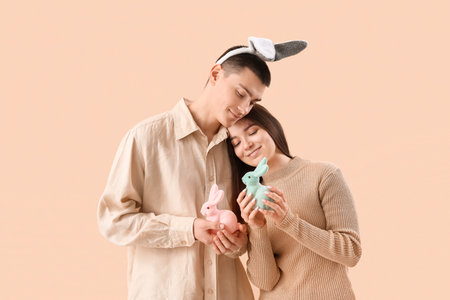 Happy young couple in bunny ears with Easter rabbits on beige backgroundの写真素材