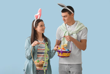 Happy young couple in bunny ears with Easter eggs on blue backgroundの写真素材