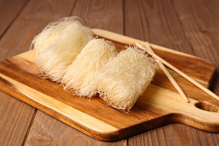 Cutting board with raw rice noodles and chopsticks on wooden board, closeup