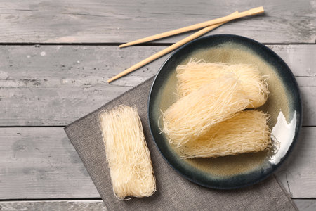 Plate with raw rice noodles and chopsticks on light wooden backgroundの写真素材