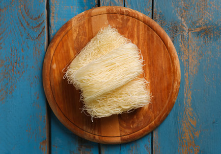 Board of raw rice noodles on color wooden background