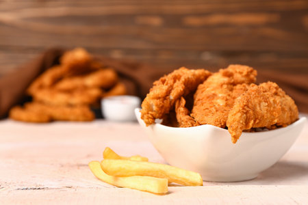 Bowl of tasty nuggets and french fries on light wooden tableの写真素材