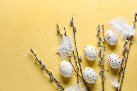 Composition with beautiful Easter eggs, feathers and willow branches on yellow background