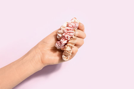 Female hand with stylish silk scrunchies on pink backgroundの写真素材