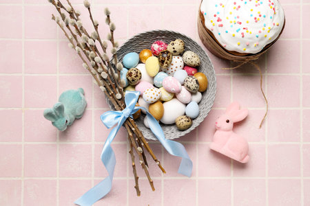 Bowl of beautiful Easter eggs, willow branches, bunnies and tasty cake on color tile