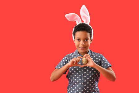 African-American little boy in bunny ears with Easter egg on red backgroundの写真素材