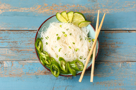 Bowl of tasty rice noodles with chili pepper on color wooden background