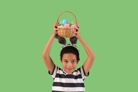 African-American little boy in bunny ears with basket of Easter eggs on green backgroundの写真素材