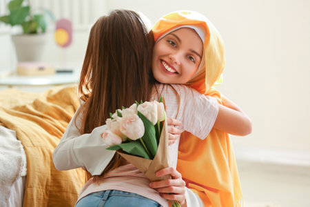 Happy Muslim woman with tulips hugging her little daughter at home on Mother's Dayの写真素材