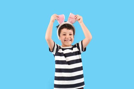 Cute little boy with bunny ears on light blue backgroundの写真素材