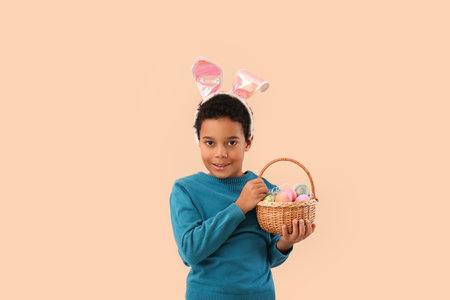 African-American little boy in bunny ears with basket of Easter eggs on beige background