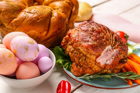 Bowl with painted eggs, tasty ham and wreath bread for Easter dinner on light wooden table, closeupの写真素材