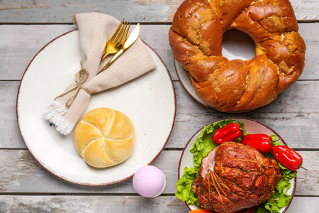 Easter table setting with tasty ham and wreath bread on light wooden backgroundの写真素材