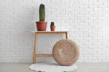 Table with green cacti and pouf near white brick wallの写真素材