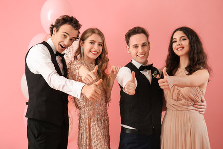 Beautiful couples dressed for prom showing thumb-up gesture on pink backgroundの写真素材