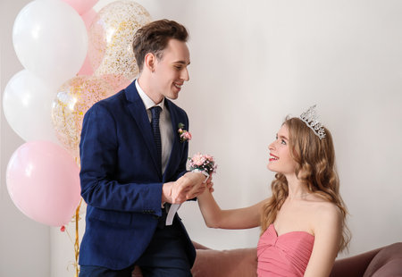 Teenage boy tying corsage around his girlfriend's wrist for prom in roomの写真素材