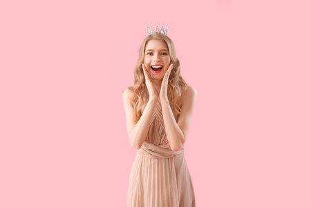 Surprised teenage girl in crown and prom dress on pink backgroundの写真素材