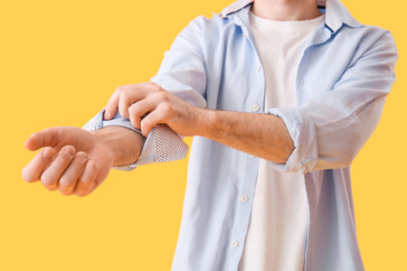 Young man rolling up his sleeve on yellow background, closeupの写真素材
