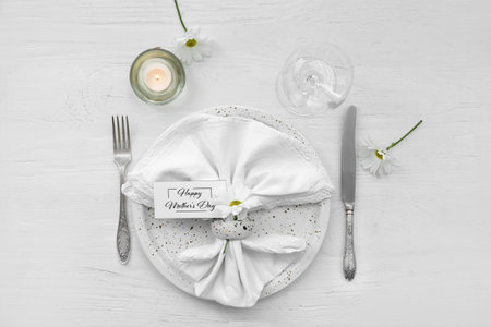 Table setting for Mother's Day celebration with daisy flowers and burning candle on white wooden...