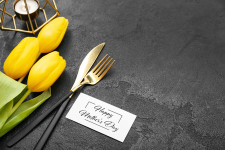 Greeting card with text HAPPY MOTHER'S DAY, cutlery and tulip flowers on black grunge background