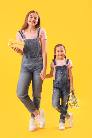 Cute little girl and her mother with gift holding hands on yellow backgroundの写真素材