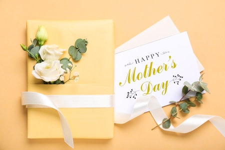 Greeting card with text HAPPY MOTHER'S DAY, gift and beautiful flowers on beige background