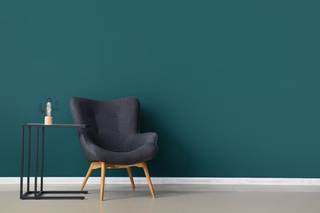 Stylish gray armchair and glowing lamp on table near green wallの写真素材