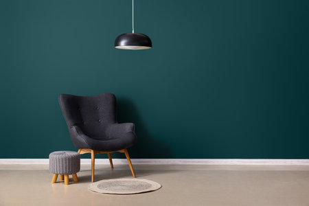 Stylish gray armchair, pouf, lamp and wicker rug near green wallの写真素材