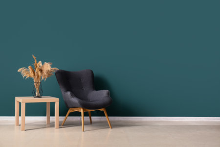 Stylish gray armchair and vase with pampas grass on table near green wallの写真素材