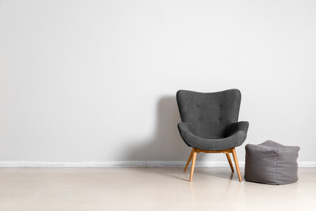 Stylish gray armchair and pouf near white wallの写真素材