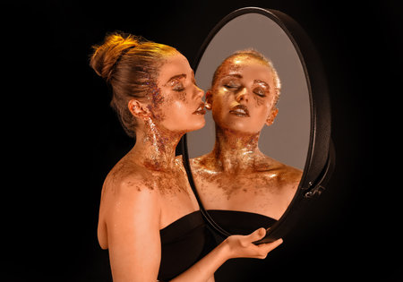 Beautiful young woman with glitter makeup and mirror on dark backgroundの写真素材