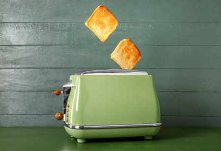 Modern toaster with crispy bread slices on green wooden tableの写真素材