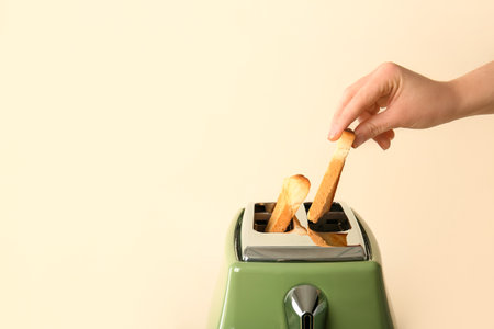 Woman taking crispy bread slice from modern toaster on beige backgroundの写真素材